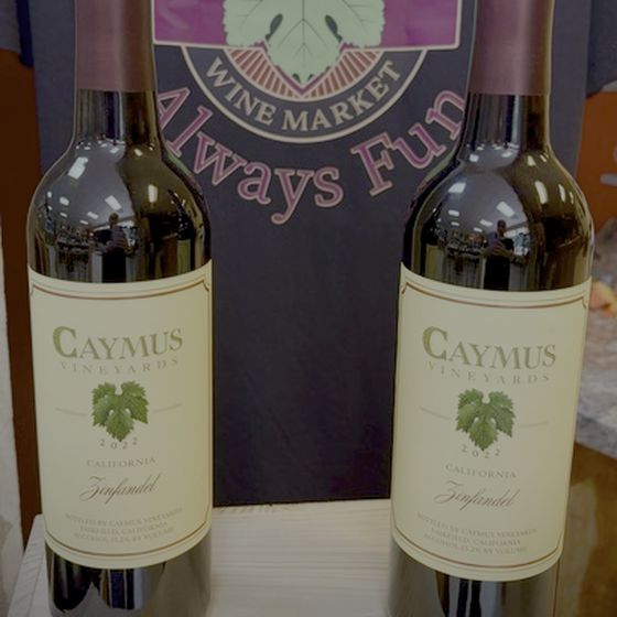 Two bottles of Caymus Vineyards California Zinfandel in front of a Bryson City Wine Market shirt