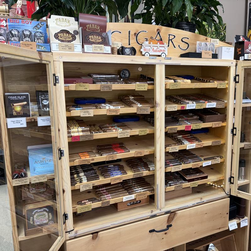 The cigar cabinet at Bryson City Wine Market, open to show rows of premium cigars beneath a hand lettered CIGARS sign