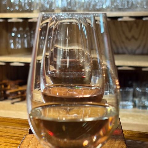 A tasting pour in a stemmed glass on the bar, with rows of hanging glassware behind