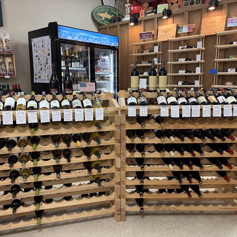 Wooden wine racks filled with bottles, with a chilled cooler and gourmet shelving behind